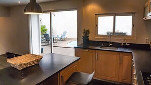 A modern kitchen with a large window, a hanging pendant light, and a view of an outdoor patio area.
