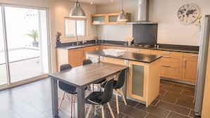 A modern kitchen with a dining area, featuring a large island, pendant lights, and a world map clock.