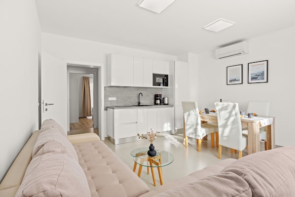 Een moderne woonkamer met een bank, een glazen salontafel, en een eethoek met stoelen en een tafel.