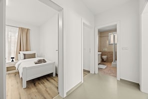 Een moderne slaapkamer met een wit bed, een nachtkastje en een raam met gordijnen.
