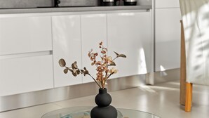A modern kitchen with white cabinets, a glass-top table, and a vase with dried flowers. - 2bedroom apartment - ground floor (Vrvari)