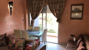 A living room with a sofa, a dining table with chairs, a glass coffee table, and a view through a door with curtains. - Appart Residence Al Menzah (Agadir)