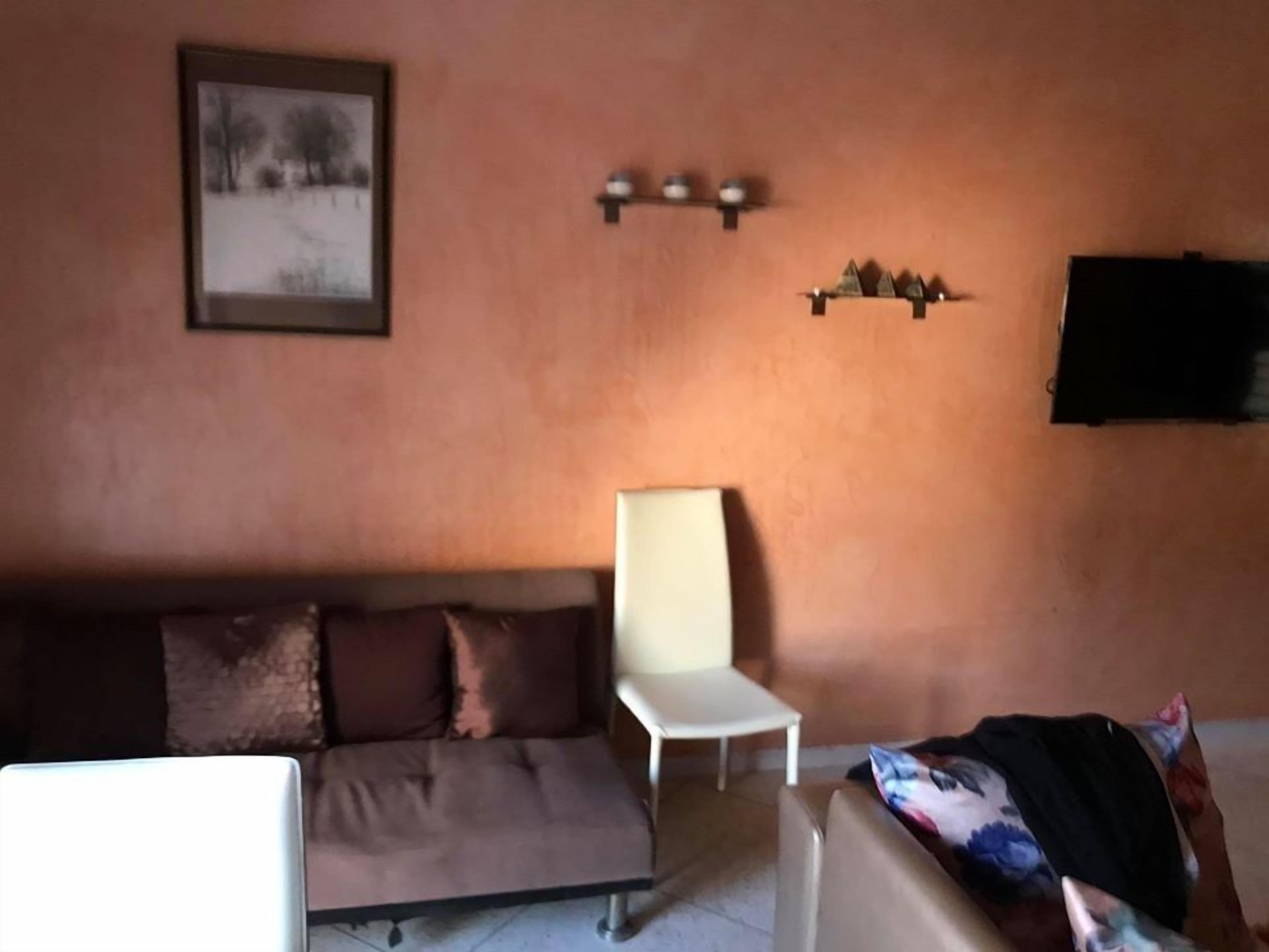 Una sala de estar con un sofá marrón, una silla blanca y un televisor montado en la pared.
