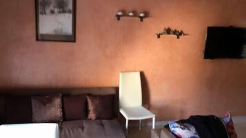 A living room with a brown sofa, a white chair, and a television mounted on the wall.