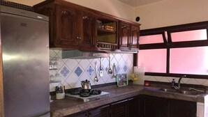 A kitchen with dark wooden cabinets, a stainless steel refrigerator, a tiled backsplash, and a window with blinds. - Appart Residence Al Menzah (Agadir)
