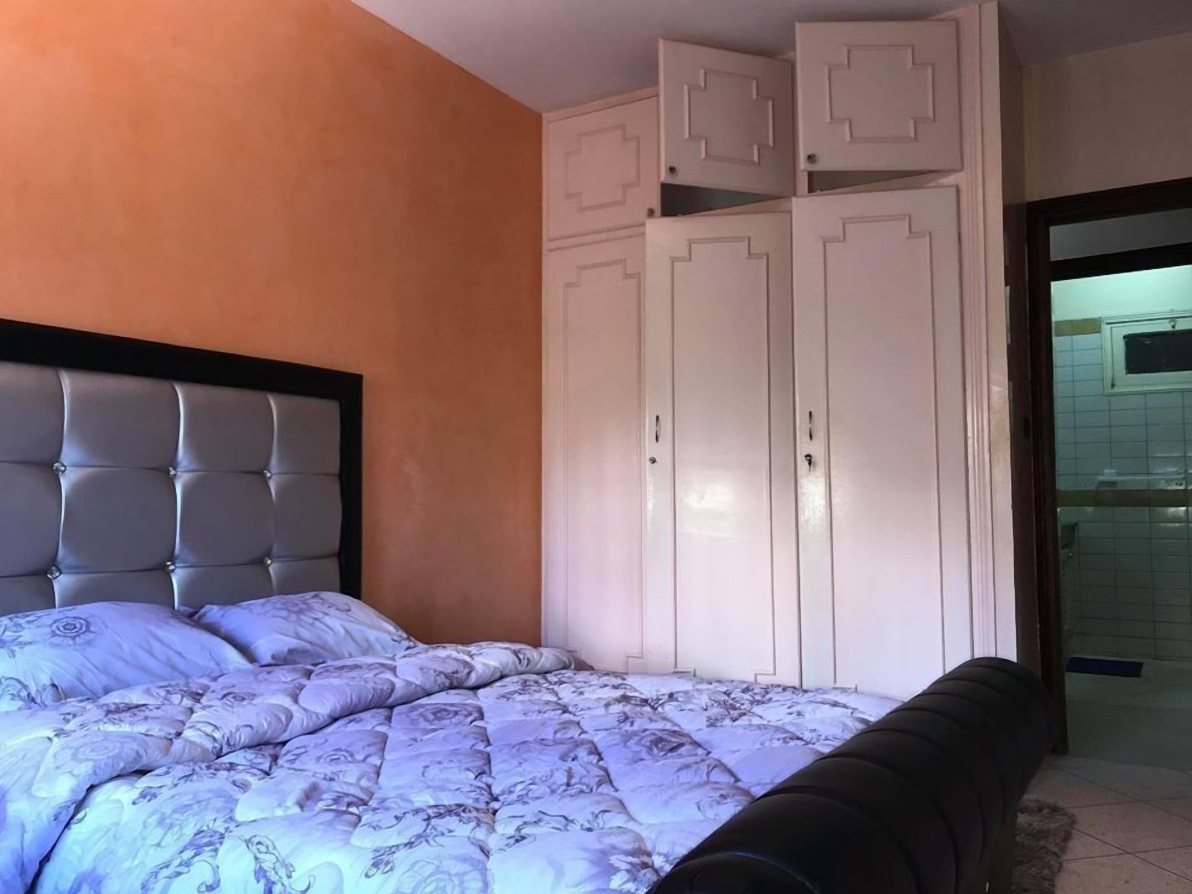 Un dormitorio con cama, cabecera, armario y baño visible a través de una puerta abierta.