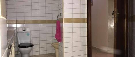 A bathroom with white tiled walls, a toilet, a sink, and a shower area.