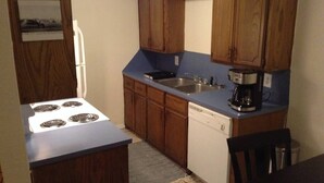 A compact kitchen with wooden cabinets, a stove, a sink, and a dishwasher. - Convenient 1-Bedroom Apartment Next to Fort Sill (Lawton)