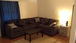 A living room with a sectional sofa, a coffee table, a side table with a lamp, and a wooden floor. - Convenient 1-Bedroom Apartment Next to Fort Sill (Lawton)