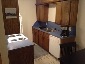 A compact kitchen with wooden cabinets, a stove, a sink, and a dishwasher. - Convenient 1-Bedroom Apartment Next to Fort Sill (Lawton)