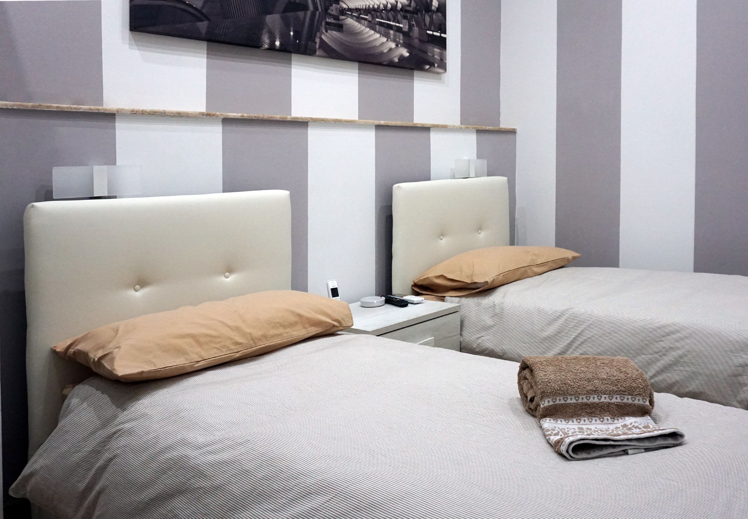 A hotel room with two beds, each with a headboard, a bedside table, and a lamp.