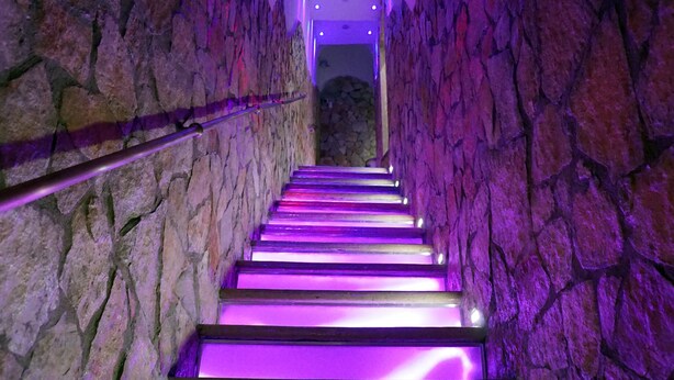 Una escalera con paredes de piedra e iluminación púrpura.