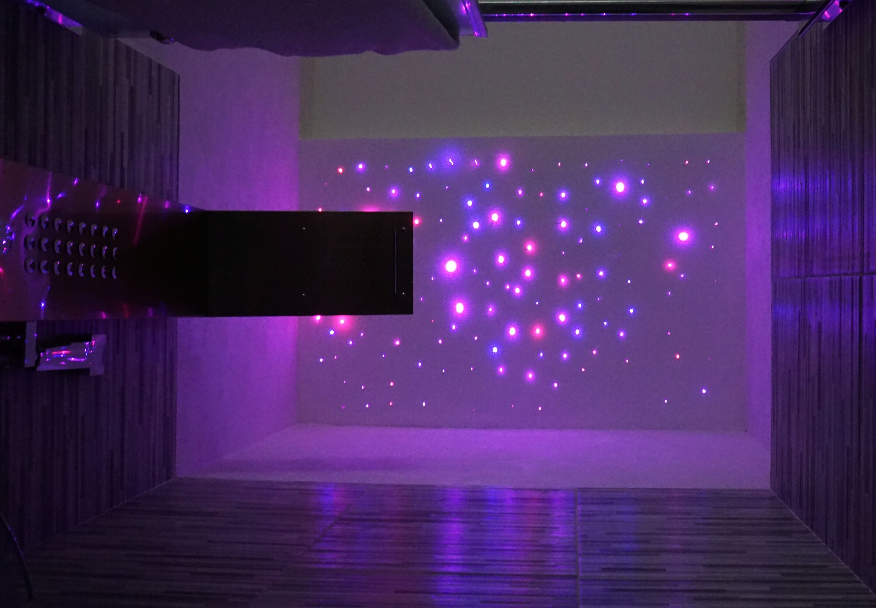 A room with a wooden floor, a projector screen, and purple ambient lighting.