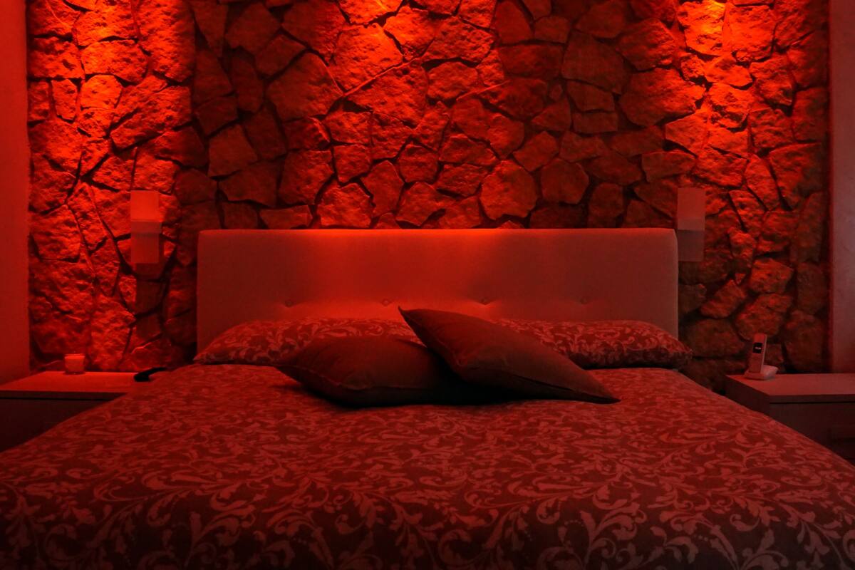A bedroom with a stone wall, a patterned bedspread, and two bedside lamps.