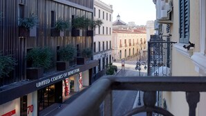 Vista de la calle con un edificio que presenta una tienda 'United Colors of Benetton', un balcón con plantas y una calle con una vista despejada de los edificios.