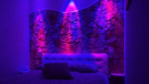 Un dormitorio con pared de piedra, cabecera tapizada y colcha estampada.