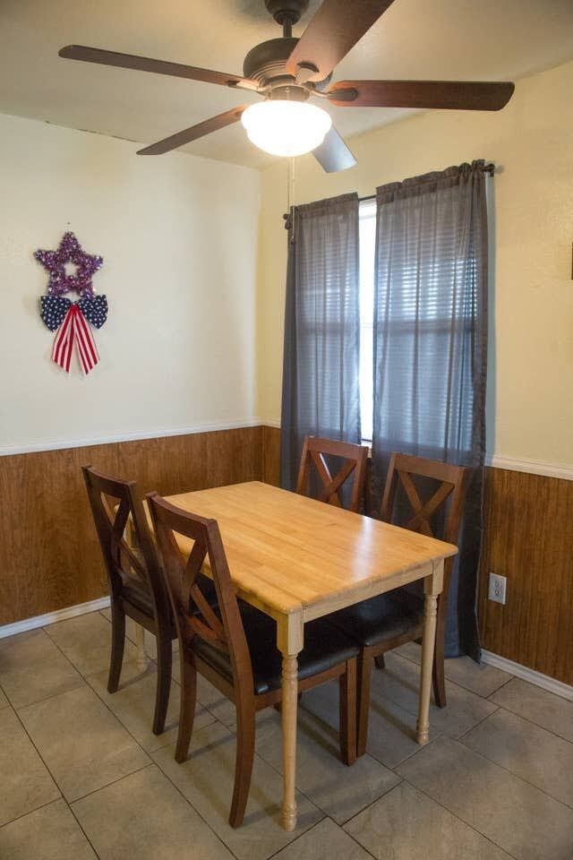 Une salle à manger avec une table et des chaises en bois, un ventilateur de plafond et une fenêtre avec des rideaux.