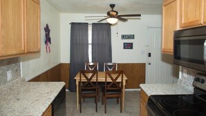 A compact kitchen with wooden cabinets, a granite countertop, a black stove, and a ceiling fan.