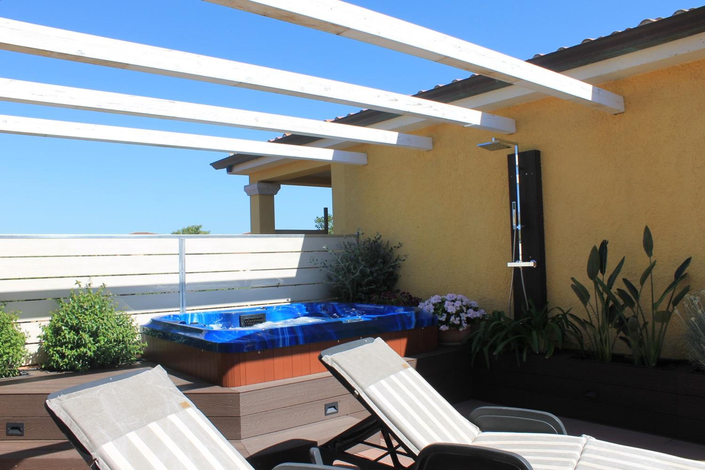 A rooftop patio with a hot tub, lounge chairs, and a pergola.