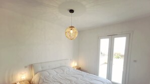 Un dormitorio con una cama grande, lámparas de noche, una lámpara de techo y un ventanal corredero al exterior.