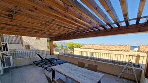 Un patio exterior con una pérgola de madera, una mesa, sillas y vistas al mar y a las montañas.