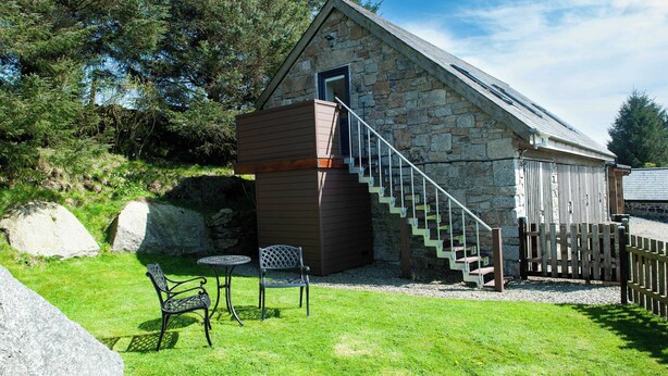 A stone building with a wooden extension, a staircase, and outdoor seating. - Dartmoor Barn on North Hessary Tor (Yelverton)