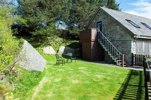 A stone building with a wooden extension, a staircase, and a grassy yard with outdoor furniture.
