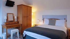 A bedroom with a bed, bedside table, lamp, wooden wardrobe, desk with mirror, and a television mounted on the wall. - Dartmoor Barn on North Hessary Tor (Yelverton)