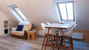 A cozy loft bedroom with a sloped ceiling, a built-in bookshelf, a comfortable sofa, a dining table with chairs, and a large skylight. - Dartmoor Barn on North Hessary Tor (Yelverton)