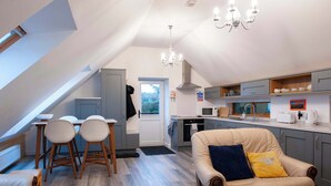A modern kitchen with a dining area, a sofa, and a staircase leading to an upper level. - Dartmoor Barn on North Hessary Tor (Yelverton)