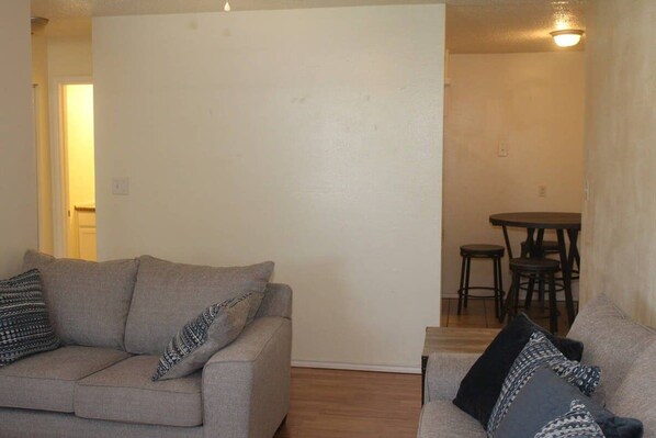 A living room with two sofas, a dining table with chairs, and a light fixture on the wall.