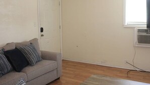 A room with a grey sofa, patterned cushions, a white door, and a window with an air conditioning unit. - 1 bedroom apartment within sight of Fort Sill (Lawton)