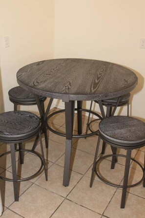 A round dining table with four stools, all featuring a dark, textured surface and metal legs.