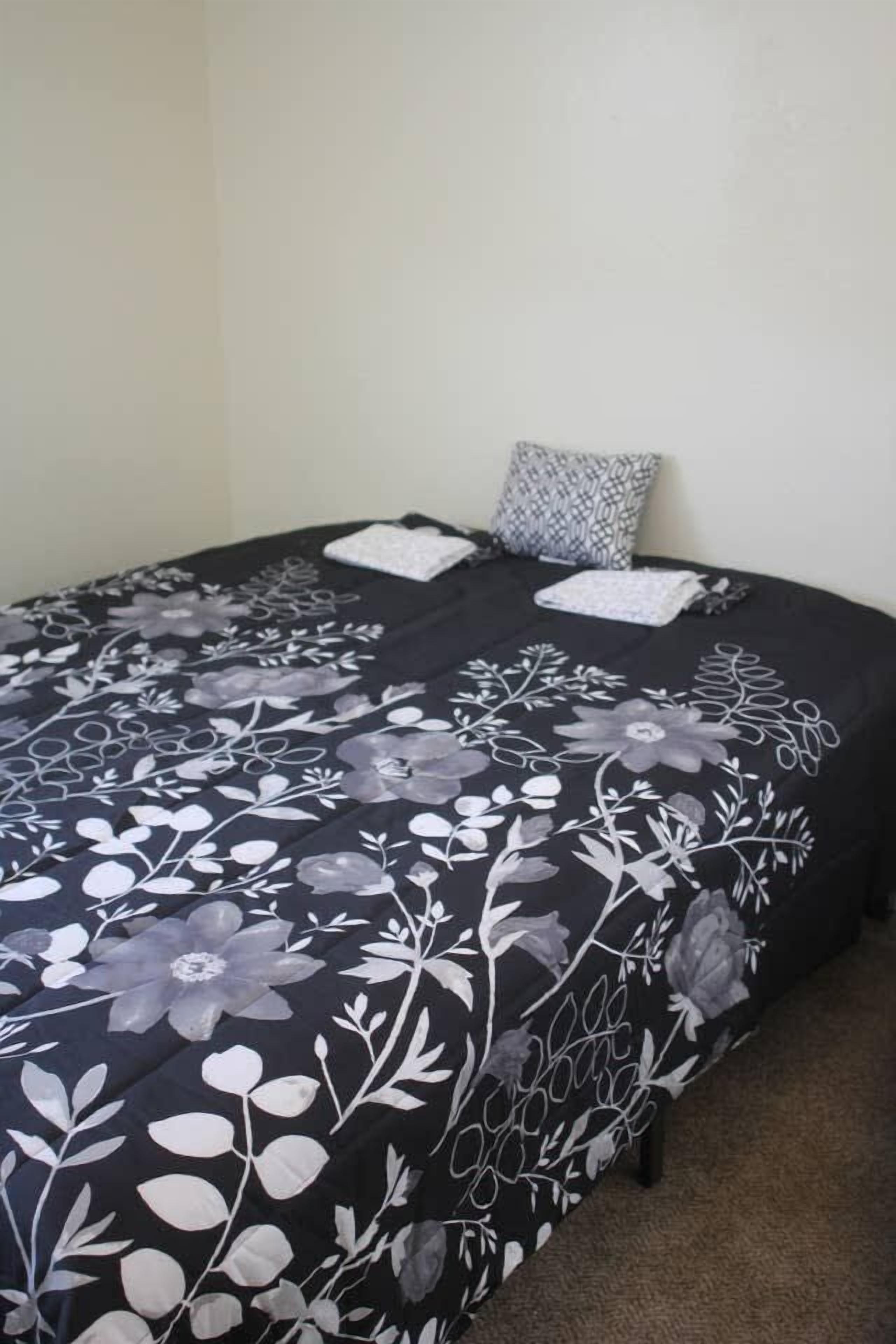 A bed with a black and white floral bedspread, two pillows, and a small bedside table.