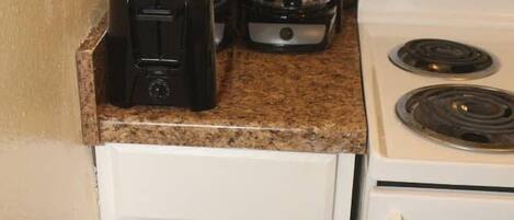 A compact kitchenette with a toaster, coffee maker, and a stove.
