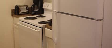 Una cocina compacta con muebles blancos, un refrigerador blanco, una estufa y una cafetera.