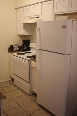 A compact kitchen with white cabinetry, a white refrigerator, a stove, and a coffee maker.
