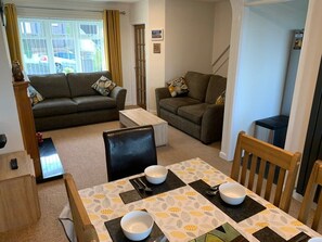 A furnished living room with a sofa, a dining table with chairs, and a view through a window. - Paignton View Holiday Home (Paignton)