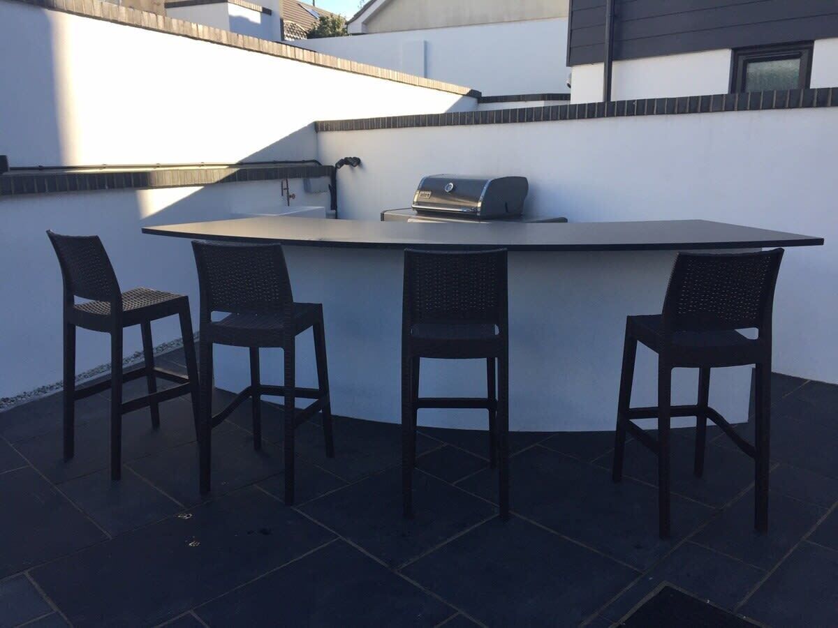 Uma área de bar ao ar livre com uma churrasqueira, duas cadeiras e uma mesa.