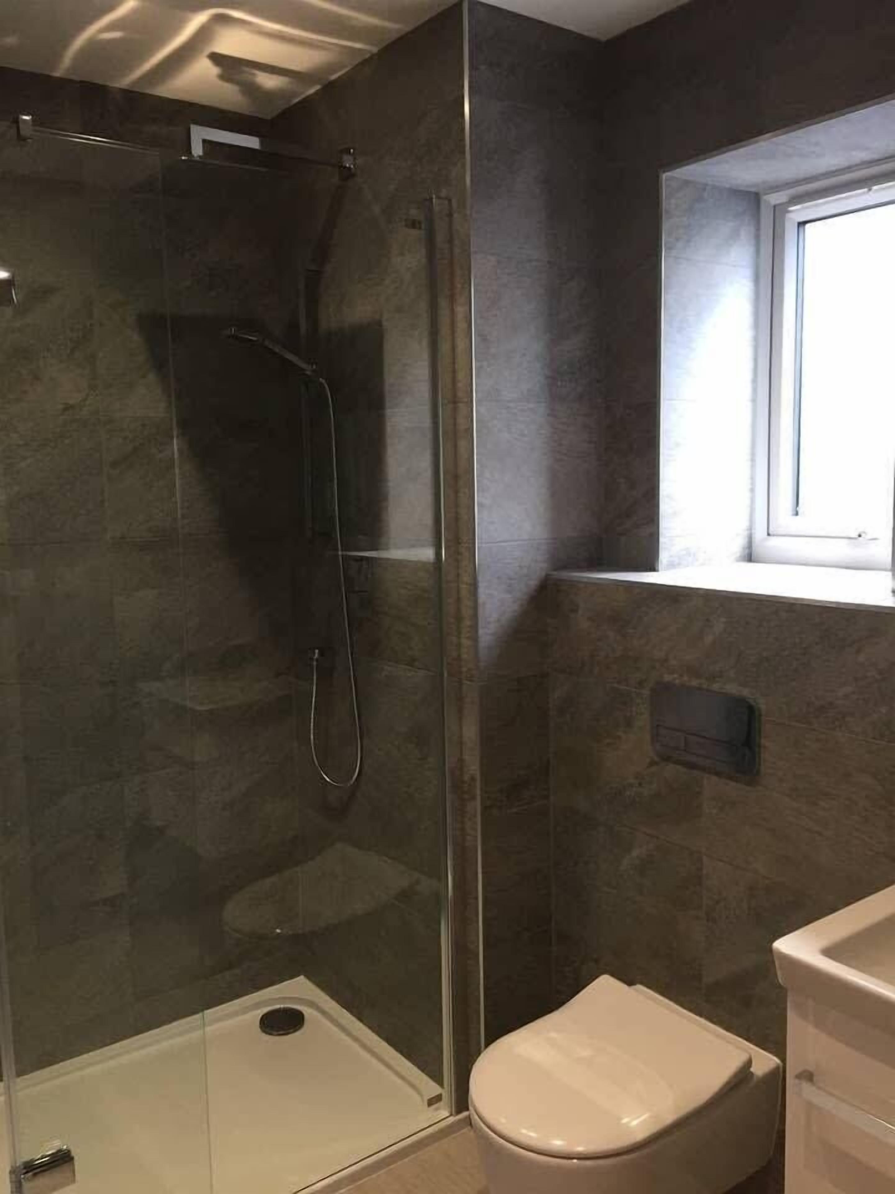 Une salle de bain avec une douche à parois de verre, des toilettes et une fenêtre au-dessus du lavabo.