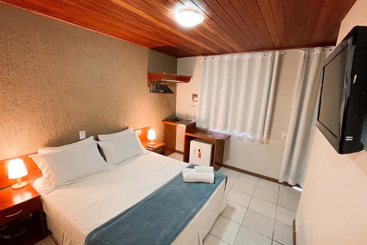 Une chambre d’hôtel comprenant un lit, des tables de chevet, un bureau, une télévision et une fenêtre avec des rideaux.
