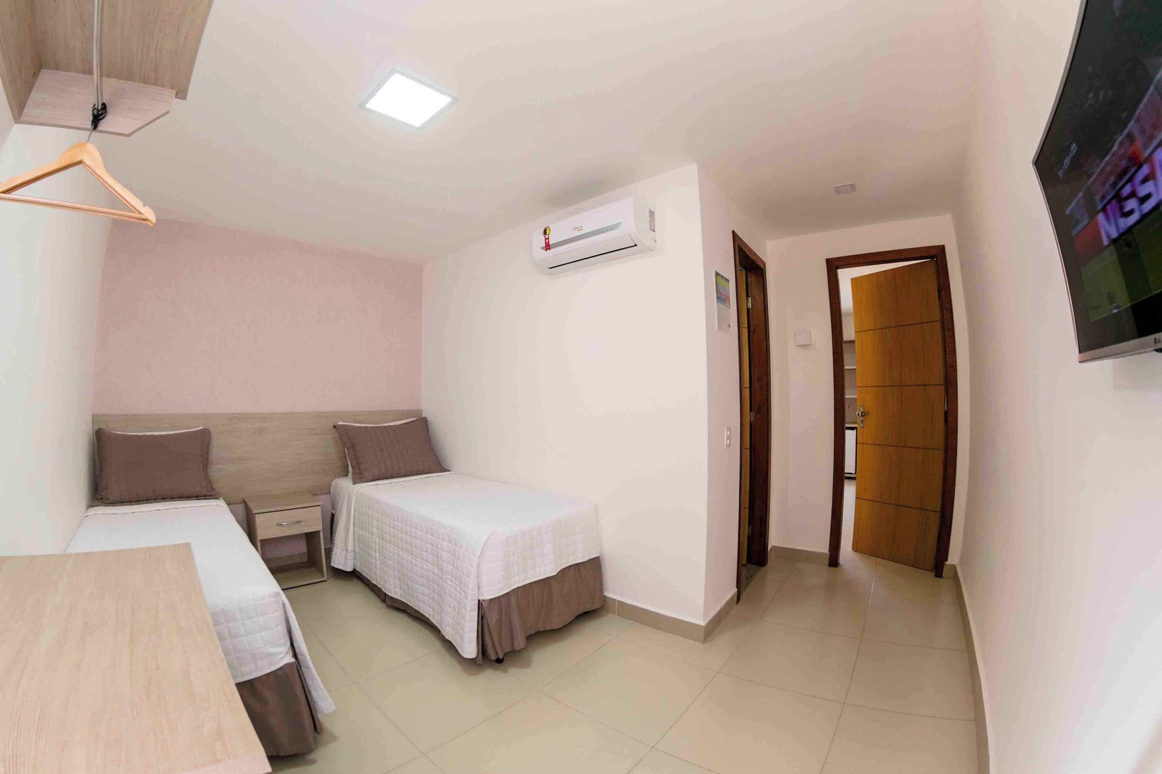 A small, clean room with two beds, a desk, an air conditioning unit, and a TV.