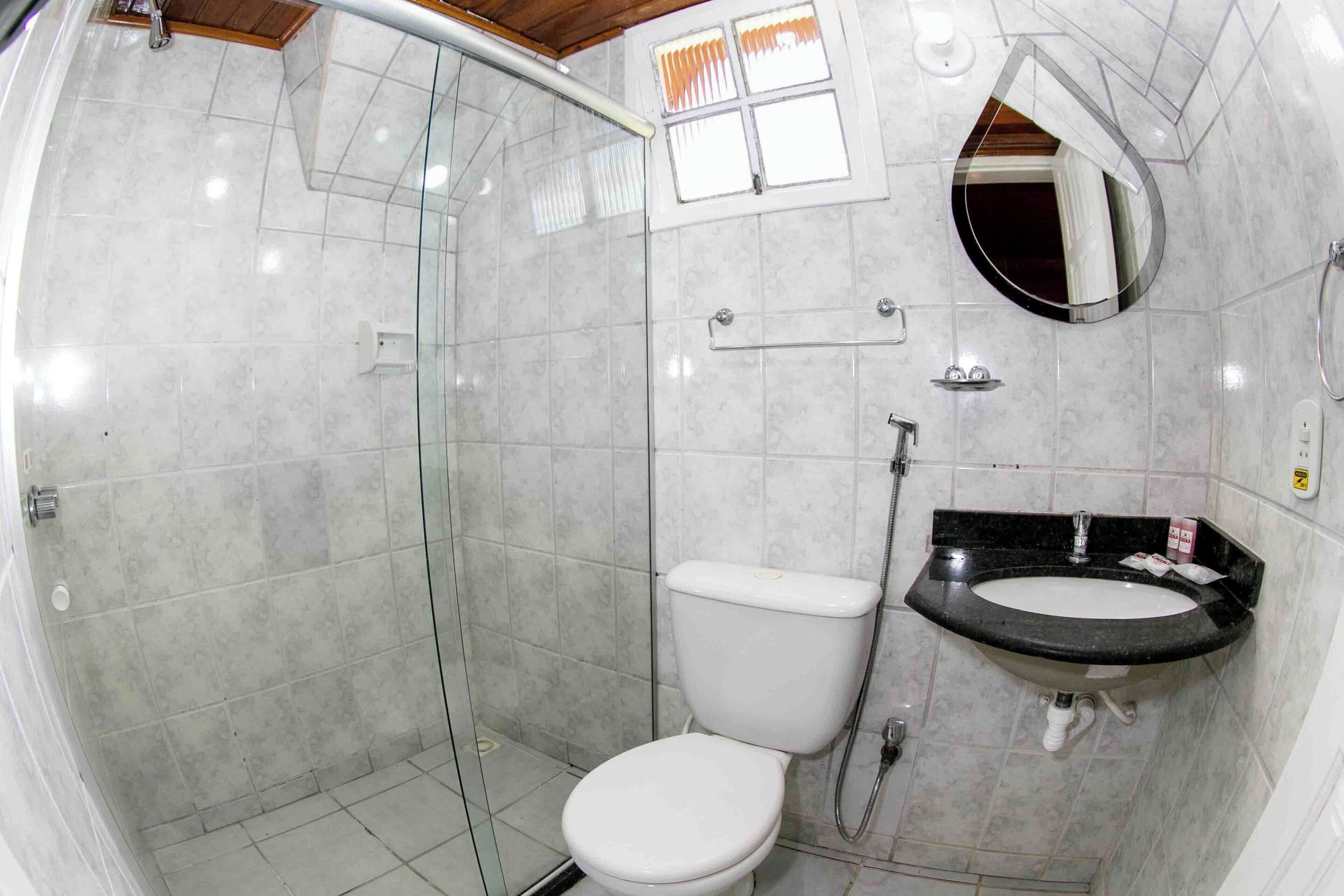 Casa de banho com chuveiro em cabine de vidro, sanita branca e lavatório com bancada preta.