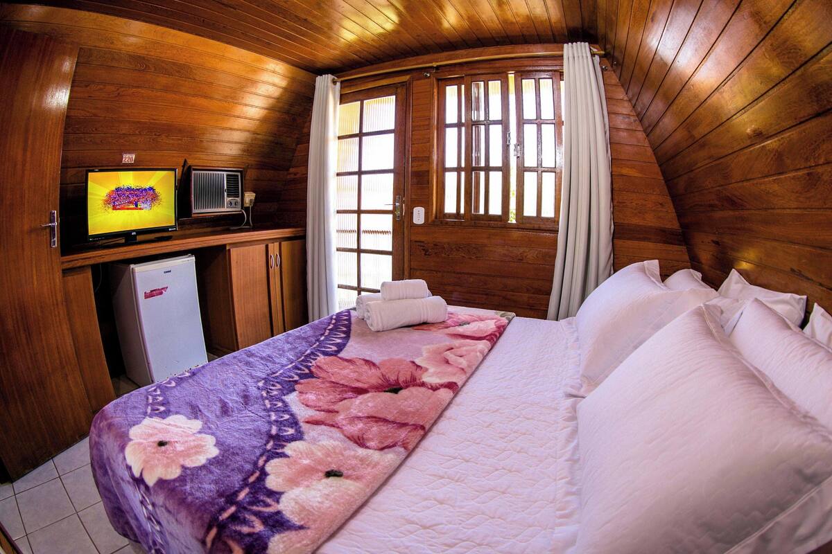 Een houten kamer met een bed, een televisie en een koelkast.
