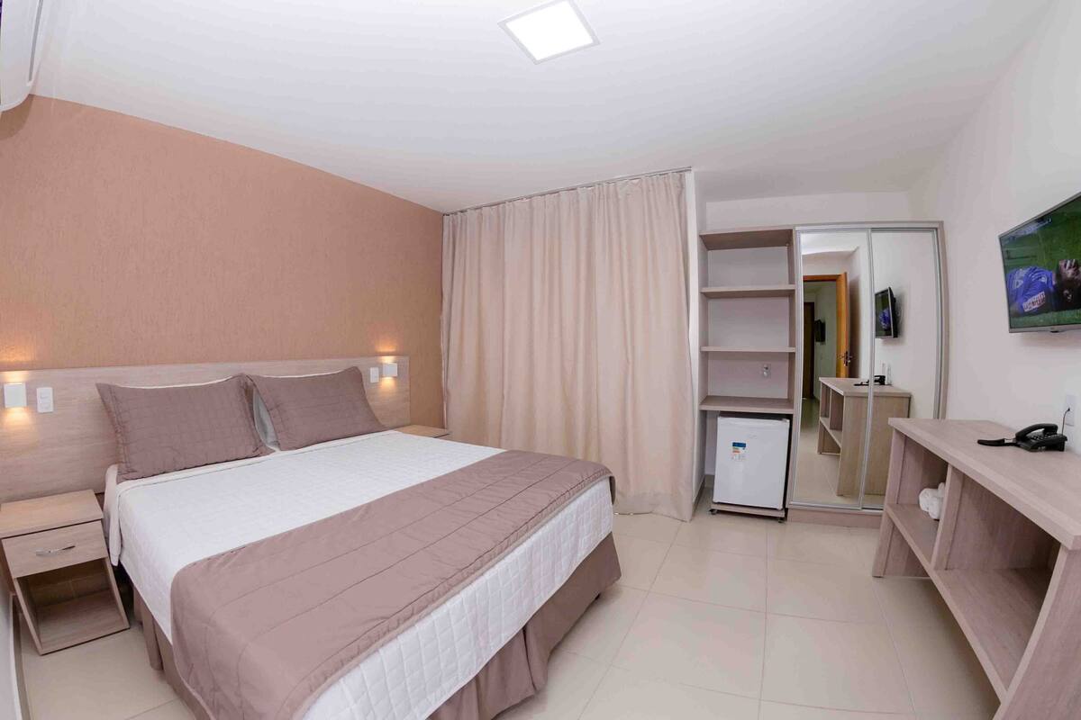 Een hotelkamer met een bed, nachtkastje, kledingkast, bureau en een televisie.