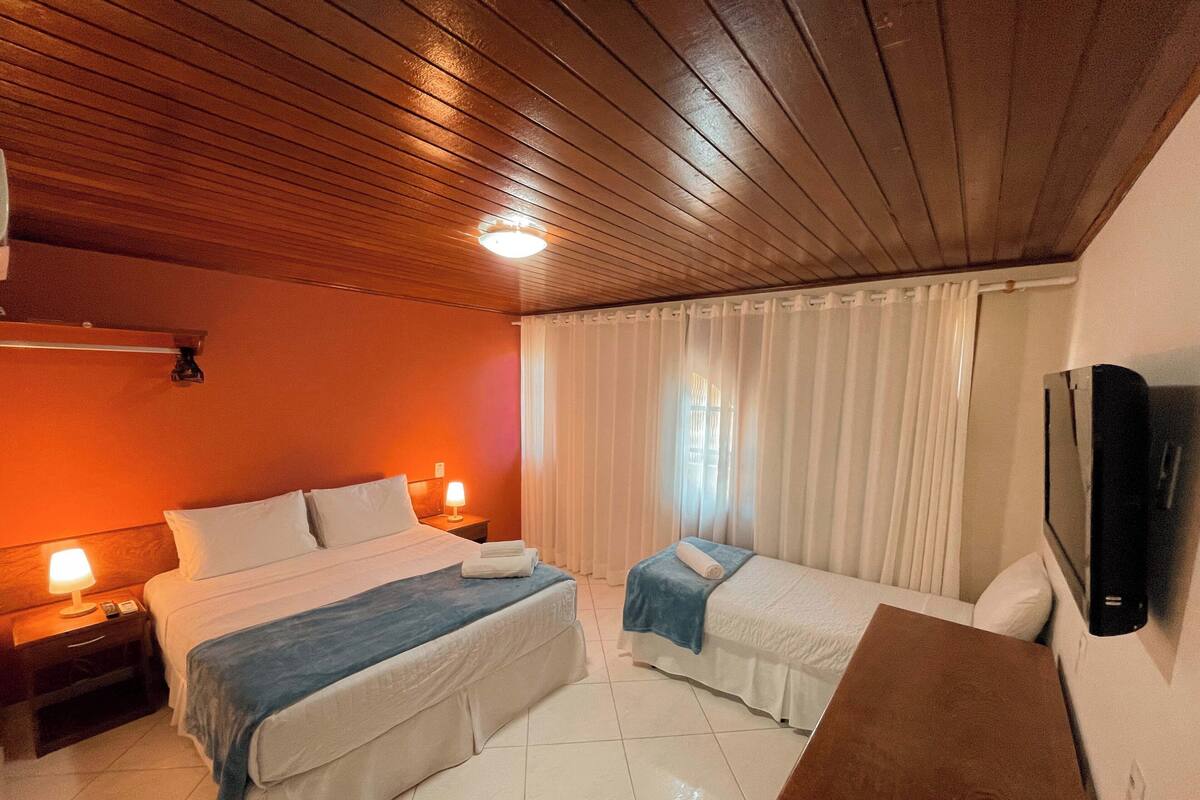 Een hotelkamer met twee bedden, een televisie en een houten plafond.
