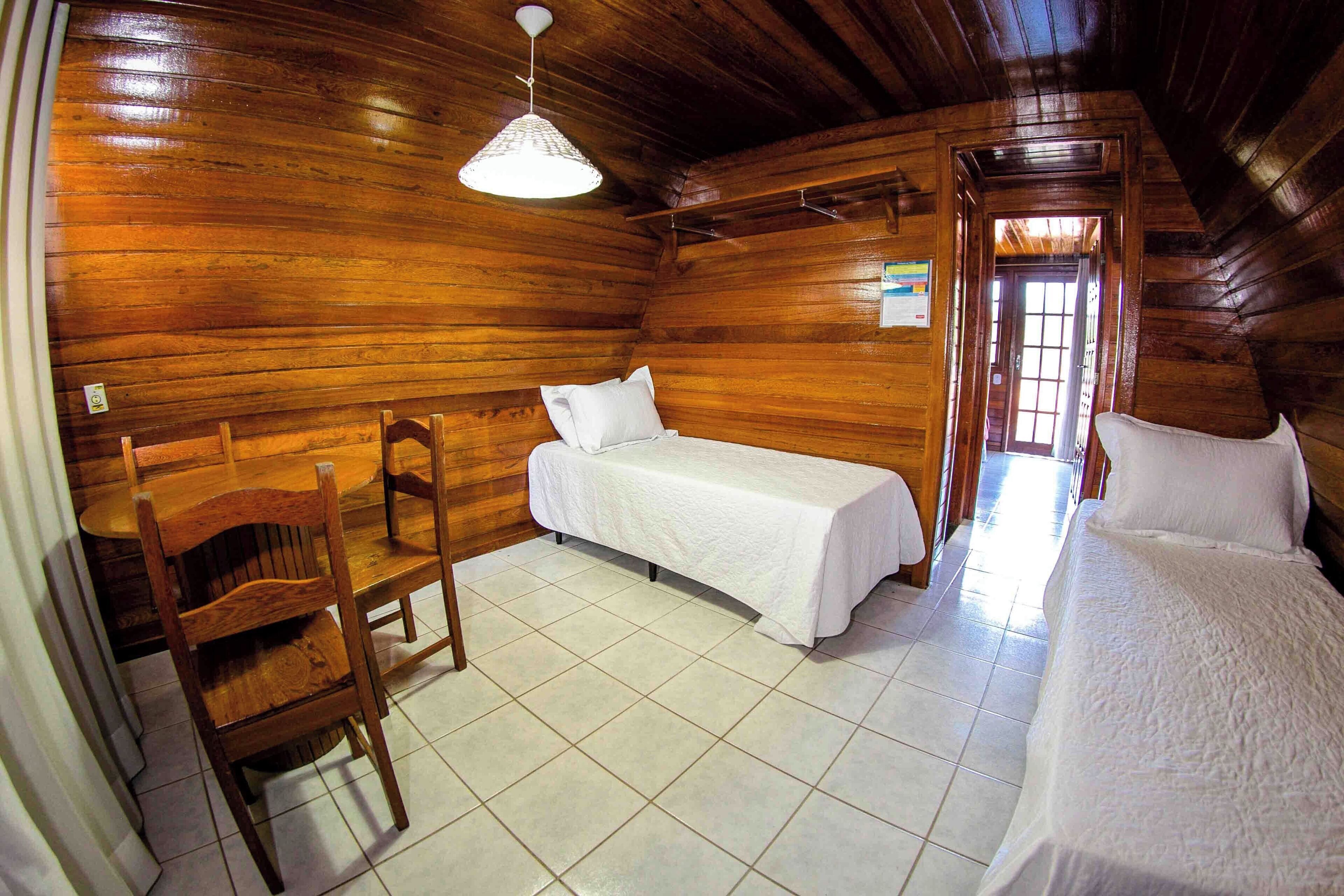 A wooden cabin room with two beds, a chair, and a table.
