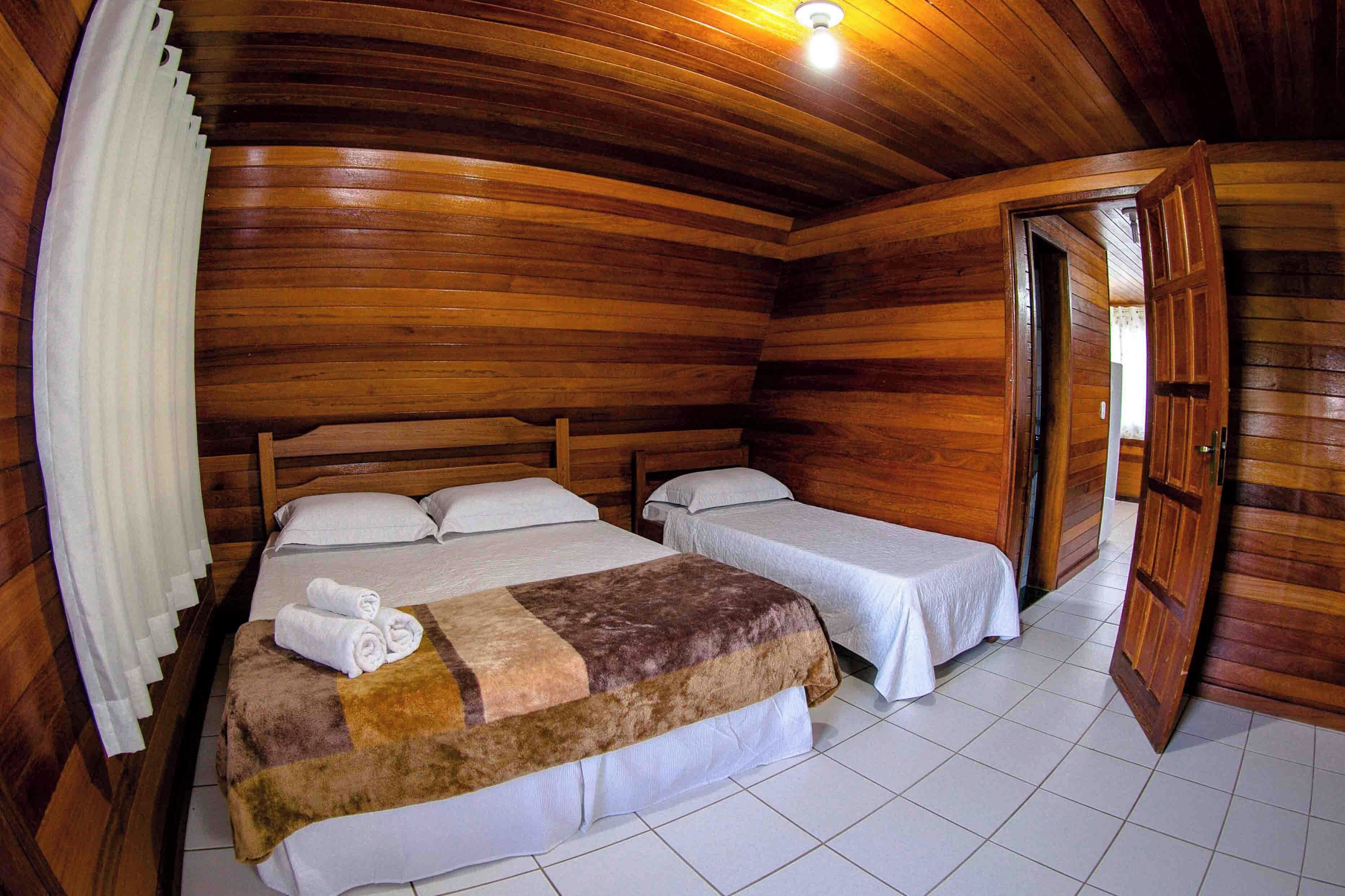 A wooden cabin-style room with two beds, a large window, and a door leading to another room.
