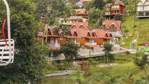 A hillside residential area with multiple houses featuring red-tiled roofs and balconies, surrounded by lush greenery and a small pond. - China Park Eco Resort (Domingos Martins)