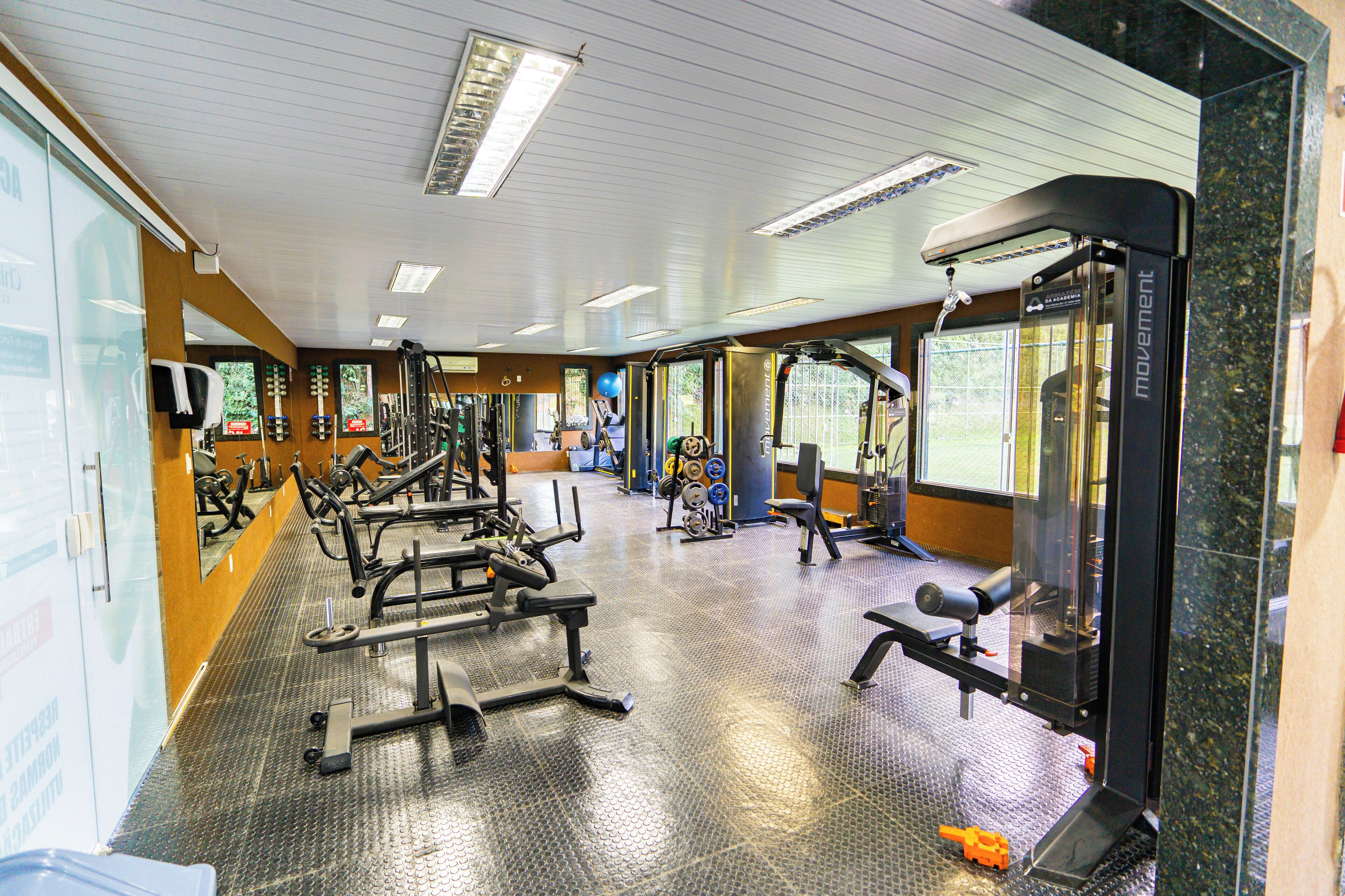 Un gimnasio con varios equipos de ejercicio, incluyendo máquinas de pesas y pesas libres, además de un espejo grande.